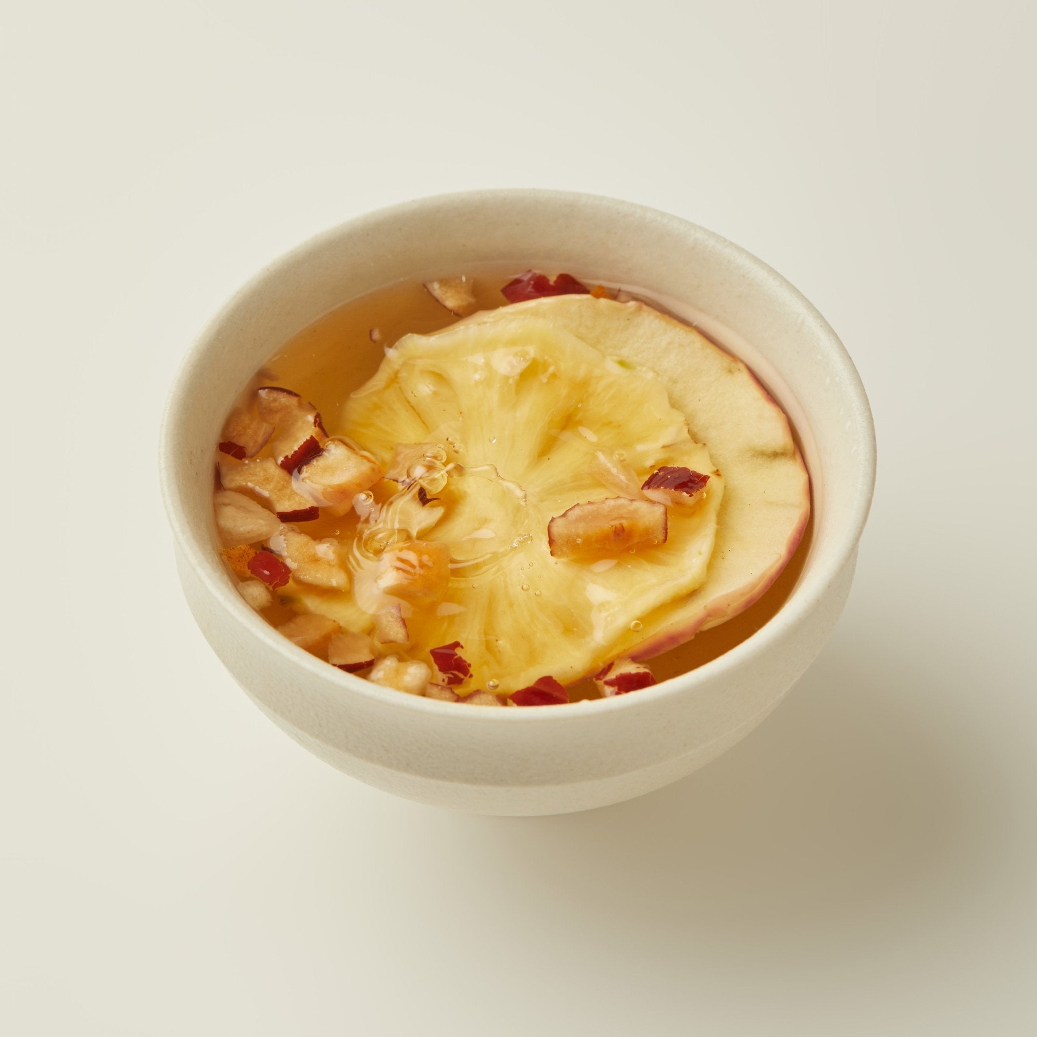 A white bowl of Chafolio Apple Pineapple Tea, no sugar, topped with a dried pineapple slice and small pieces of dried fruit.
