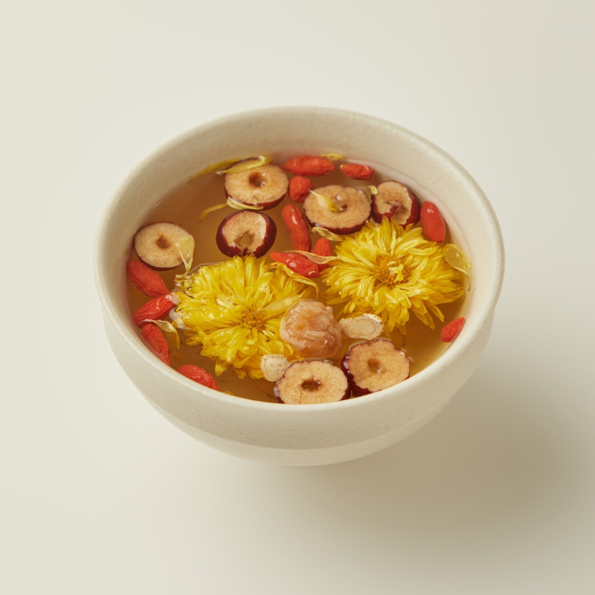 A cup of Chafolio Chrysanthemum Ginseng Tea featuring yellow chrysanthemum flowers, goji berries, jujube slices, and lotus seeds floating on top.