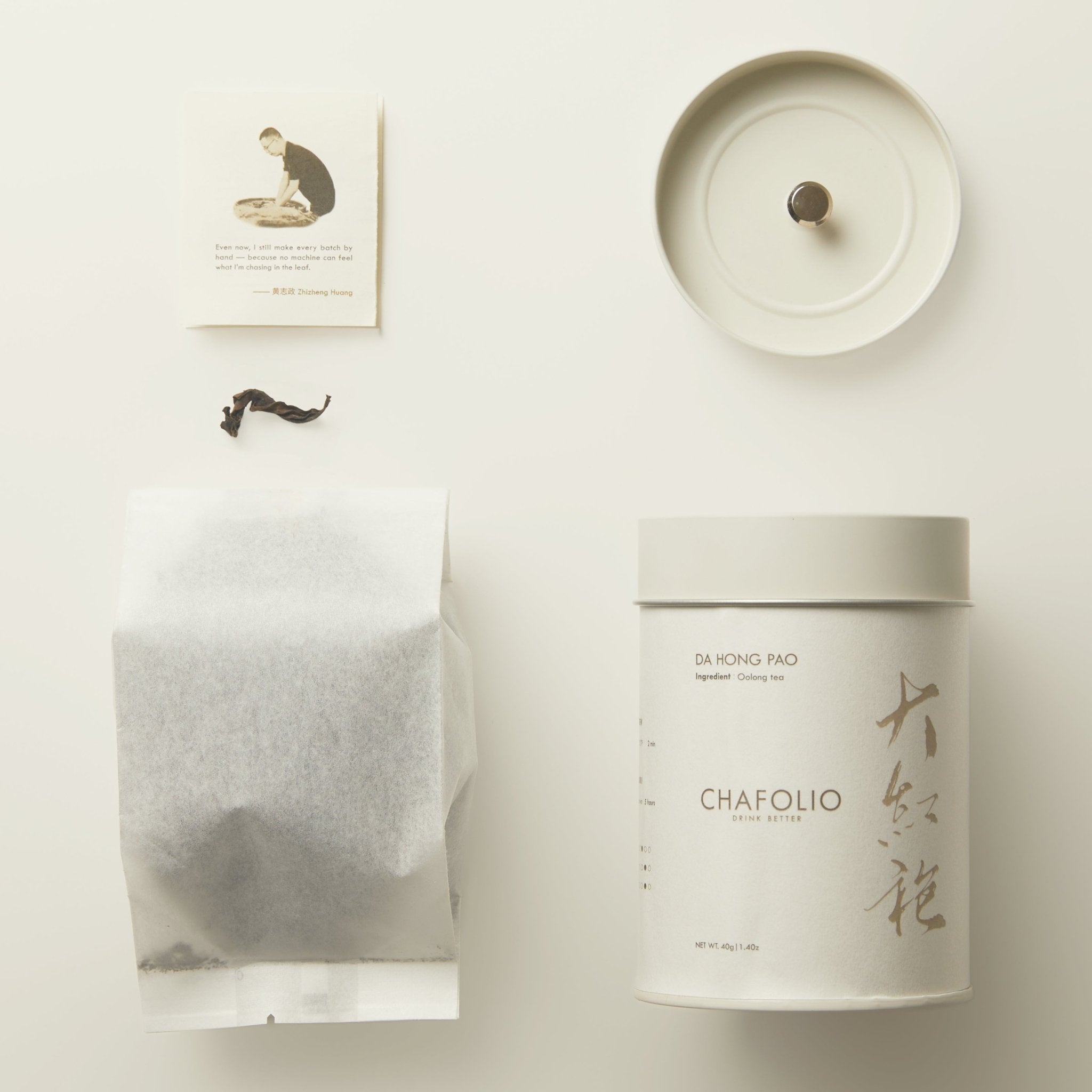 A white Chafolio canister labeled "Da Hong Pao — Craftfolio," along with a tea bag, canister lid, and illustrated info card, are neatly arranged on a light surface, capturing the elegance of Wuyi Mountains Da Hong Pao oolong tea.