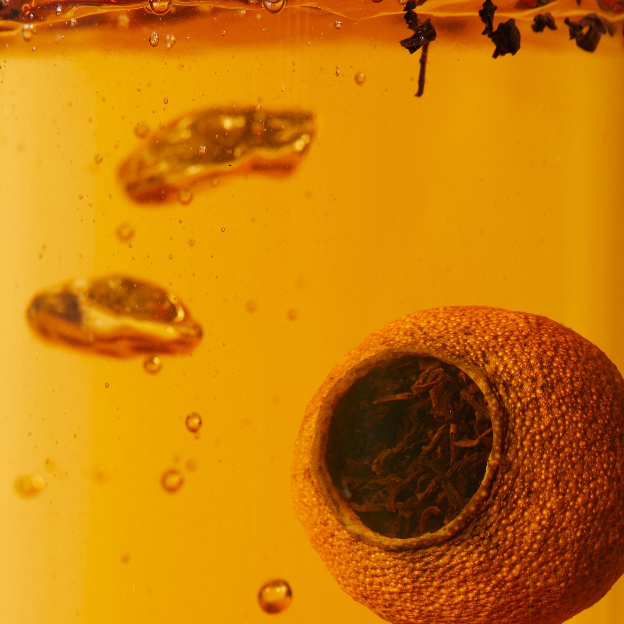 Close-up of Chafolio Tangerrine Pu'er: a hollowed green tangerine peel filled with pu-er tea leaves, steeped in amber liquid with bubbles and floating tea leaves.