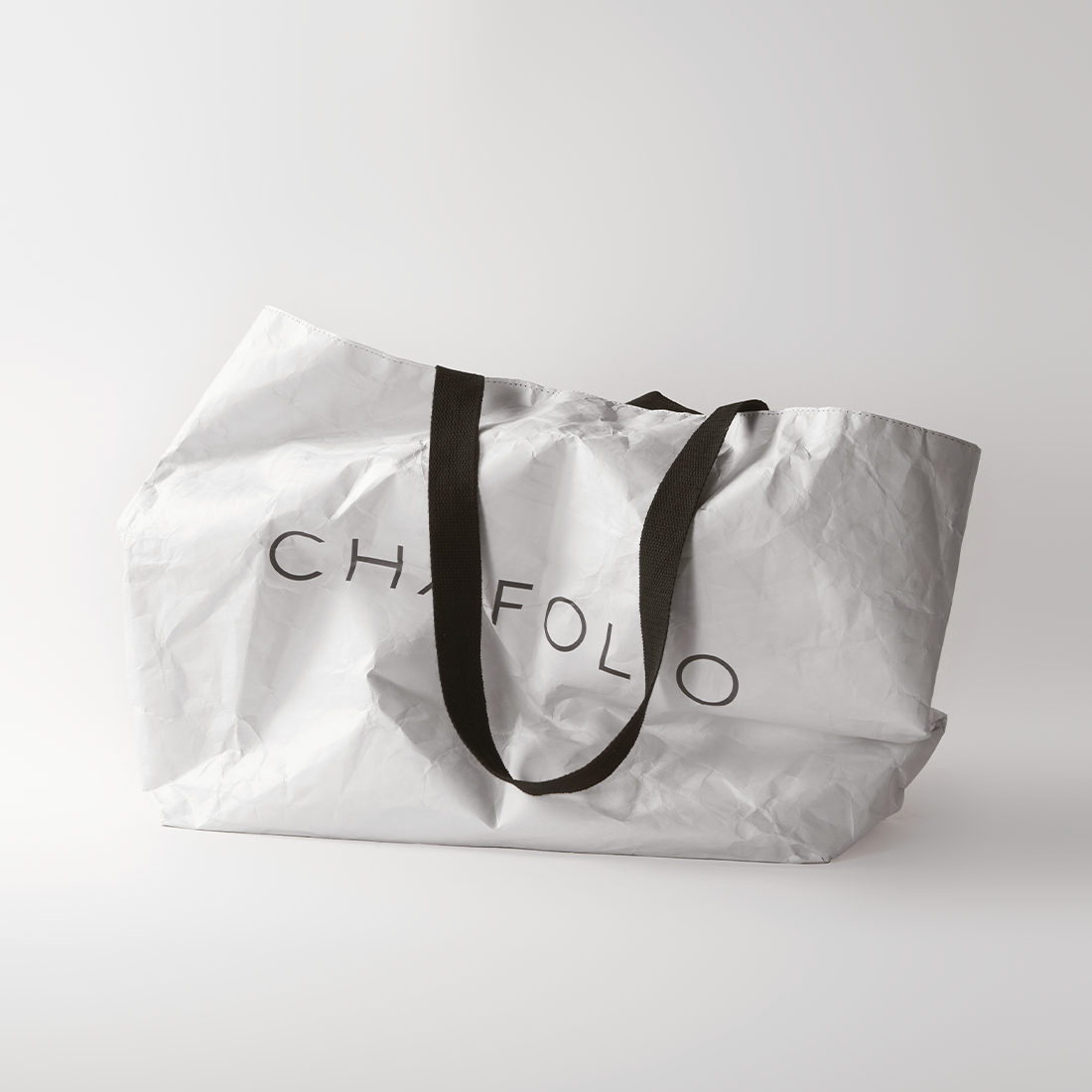 A white Tyvek Tote Bag by Chafolio with black handles and partially visible "CHAFOL" text is shown against a plain white background.