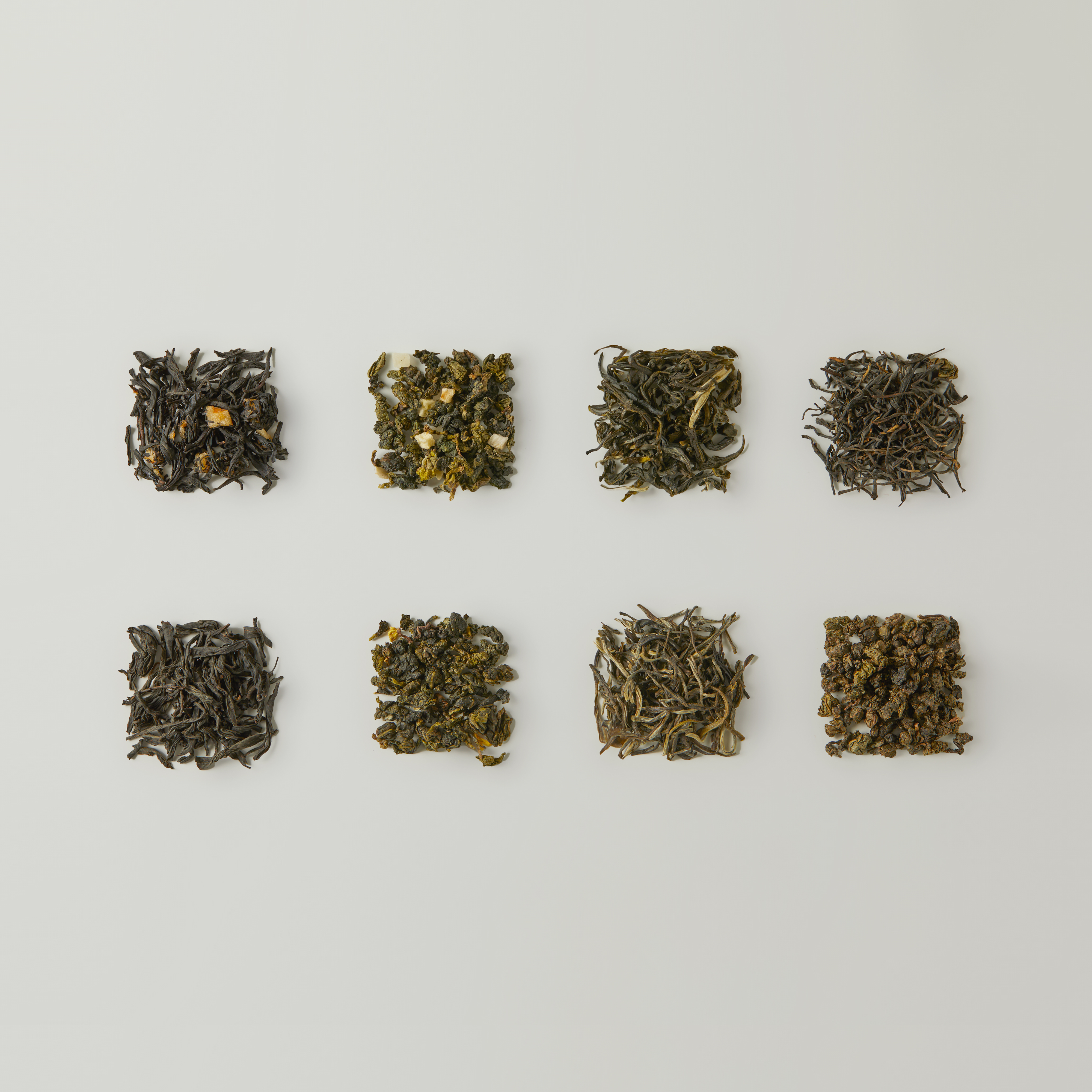 Eight small piles of loose leaf teas from Chafolio's Discovery Set | Curated Tea Selection, including Oolong and Jasmine Green Tea, are neatly arranged in two rows on a plain white background.