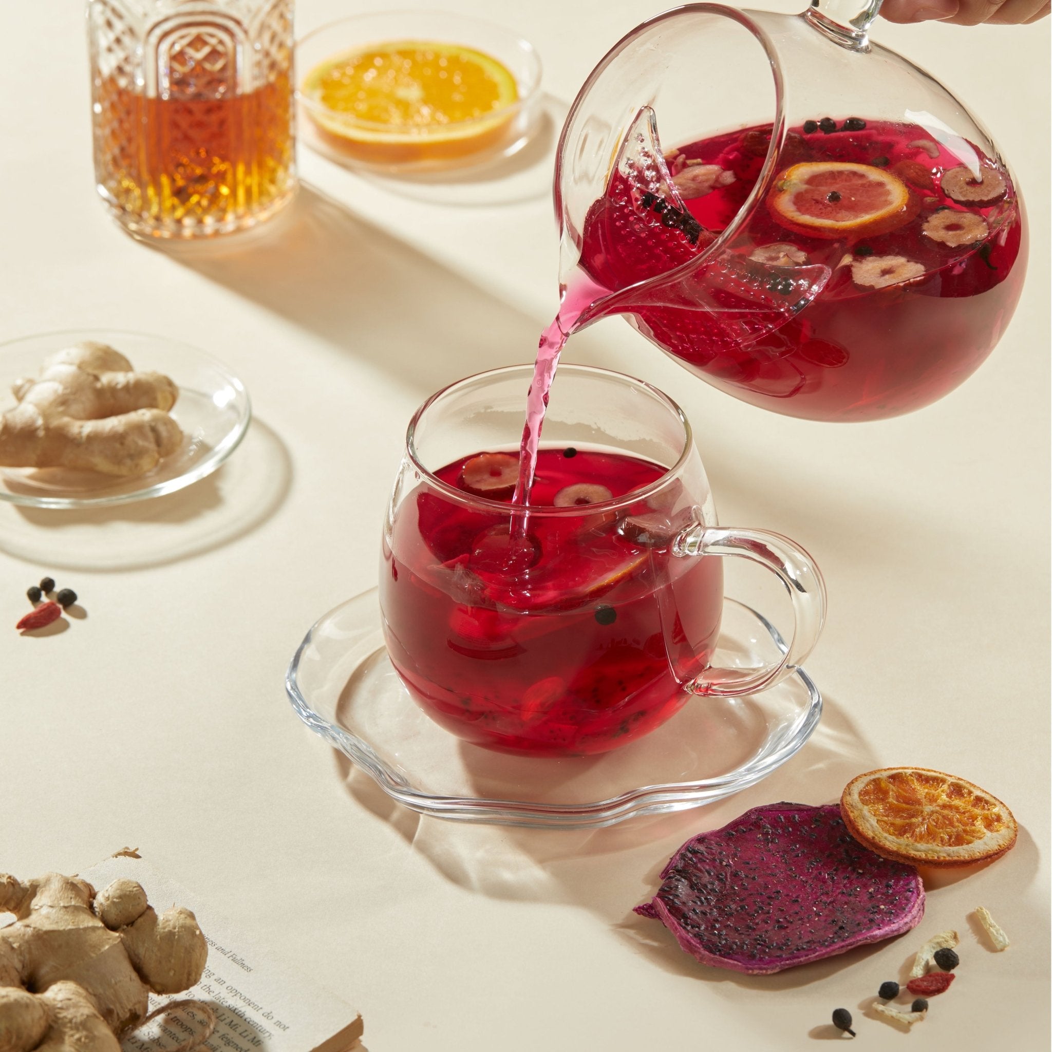 Chafolio’s Dragonfruit Ginger Tea pours vibrant red tea with citrus and berries into a glass cup; ginger and orange slices nearby showcase this blend’s natural digestive support.