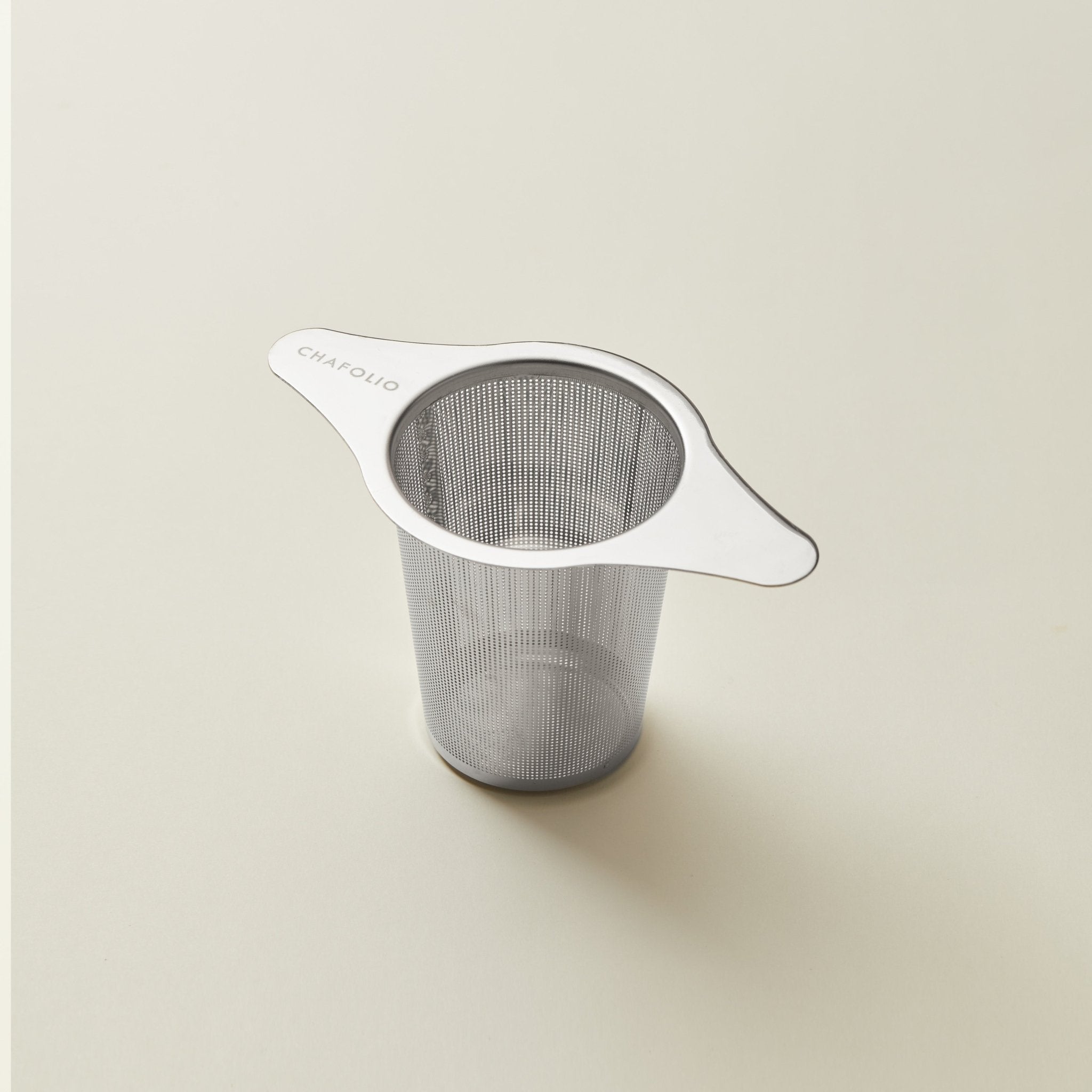 The Chafolio Ear-hanging Tea Infuser, made of stainless steel and featuring two handles, rests on a plain light surface.