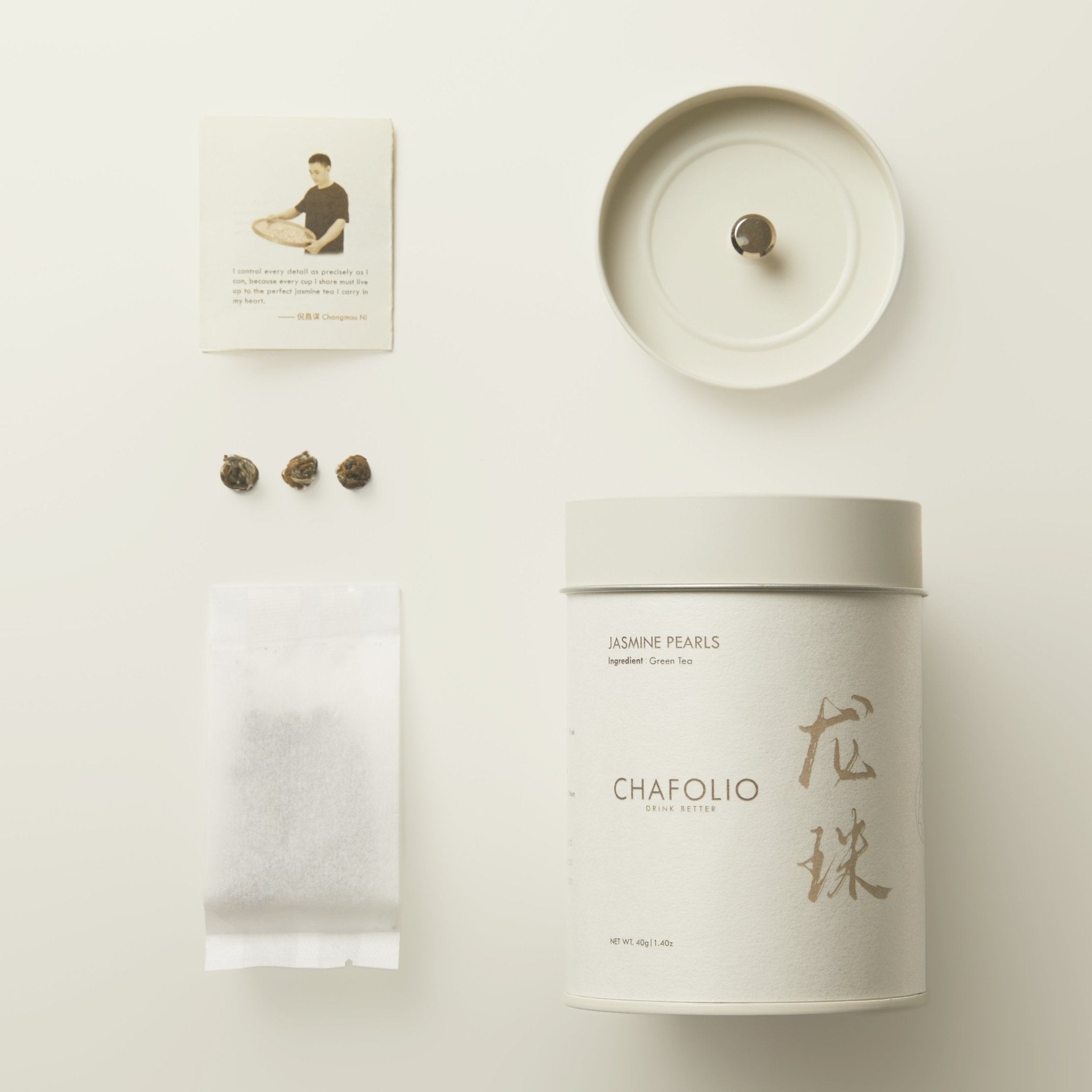 A white tin labeled "Jasmine Pearls — Craftfolio" by Chafolio, with a lid, three tea pearls, a tea bag, and an instruction card are arranged neatly on a white surface.